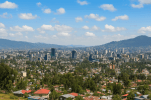 Aerial view of Addis Ababa city skyline with modern buildings, green hills, and mountains in the background under a bright blue sky.